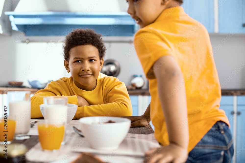 Good morning. Charming pre-teen boy sitting at the table and having breakfast while his younger brother joining him at the table Good morning. Charming pre-teen boy sitting at the table and having breakfast while his younger brother joining him at the table