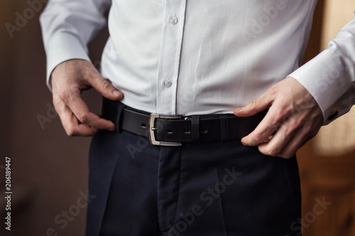 Businessman putting on a belt, fashion and clothing concept,groom getting ready in the morning before ceremony