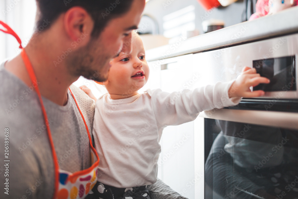 Young father cooking and takes care of little child in the kitchen at home Young father cooking and takes care of little child in the kitchen at home