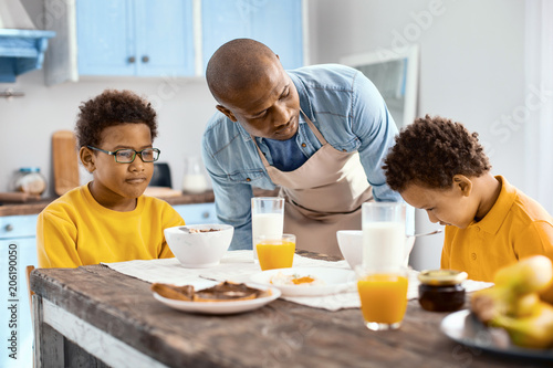 What is wrong. Loving young father talking to his upset son, asking him what is wrong, while they having breakfast