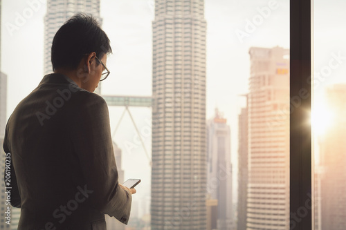 Malaysian business man contact to customer by wifi and smart phone in hotel room with Kuala lumpur city background, Kuala lumpur, Malaysia