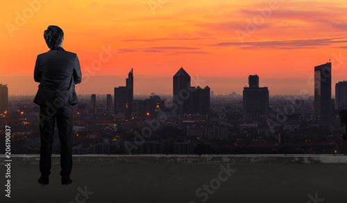 Businessman standing on roof and looking at Cityscape skyline night light