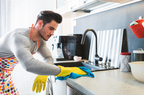 Billede på lærred Handsome man in yellow gloves cleaning kitchen, modern masculinity