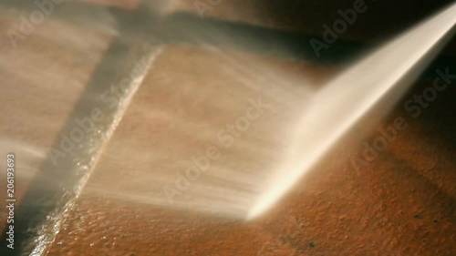 Closeup on cleaning outdoor floor ceramic tiles with high pressure water washer. Water sprinkling and shining in evening sunset. Spring cleaning arround the house.