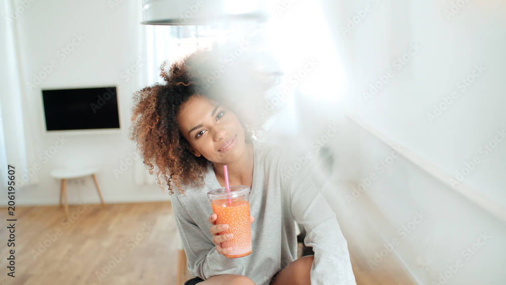 Happy mixed race woman holding smoothie, looking to camera. Happy mixed race woman holding smoothie, looking to camera.