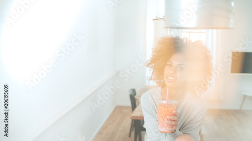 Happy mixed race woman holding smoothie, looking to camera.