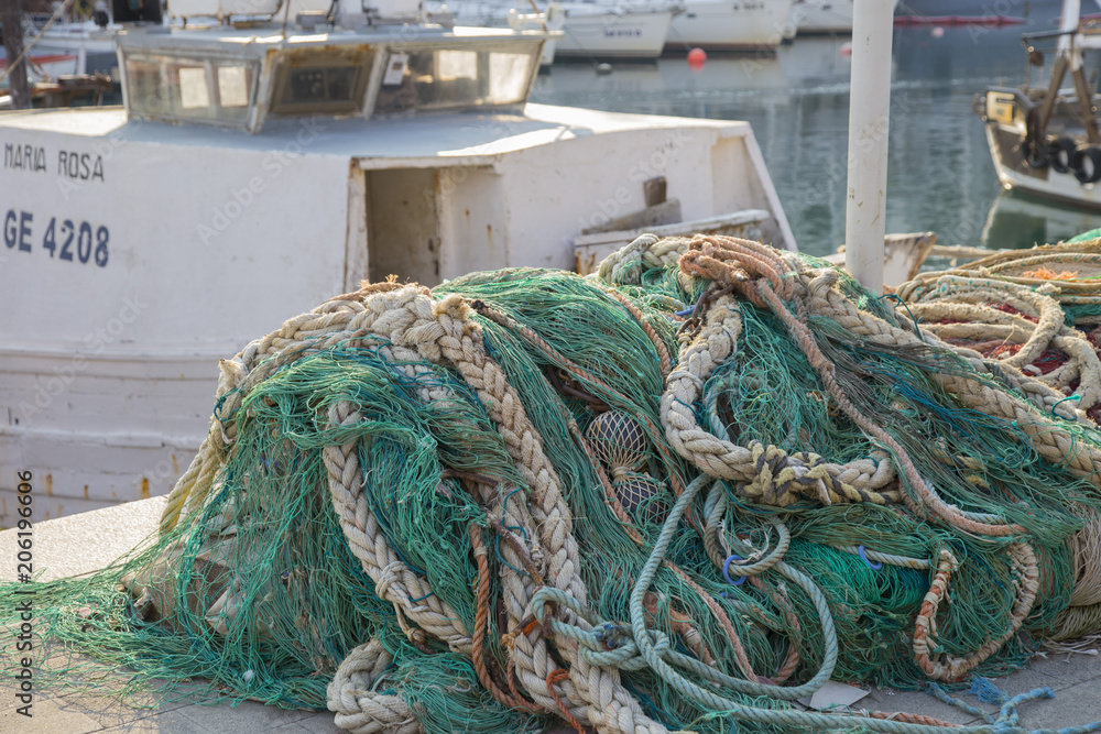 Heap of fishing nets on a quay in a harbour with a small fishing boat visible behind in a close up view