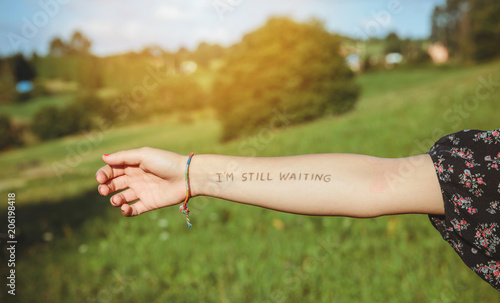 Closeup of female arm with the text -I'm still waiting- written in the skin over a nature background