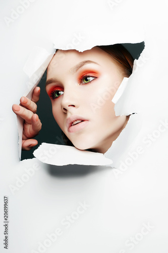 Face of girl with make-up into a hole in paper