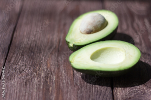 green avocado cut into halves on a wooden table with a shallow depth of field