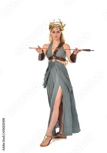 full length portrait of pretty blonde lady wearing fantasy toga gown, and holding a bow and arrow. standing pose on white background.