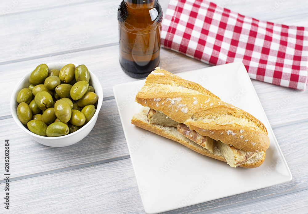 Omelet sandwich with potatoes next to bowl with olives and a beer on wooden table. Typical spanish food. Omelet sandwich with potatoes next to bowl with olives and a beer on wooden table. Typical spanish food.