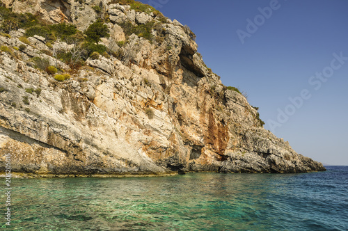 Beautiful and colorful view of rock coastline and crystal, blue sea on sunny day. Small stone cliff ideal for jump into turquoise water during vacation trip. © less.talk