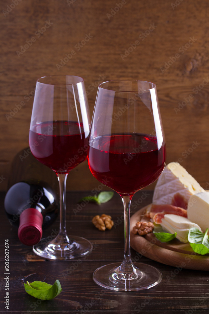 Glasses and bottle of wine with cheese, bread, nuts and jamon or prosciutto on dark wooden background. Wine and food concept