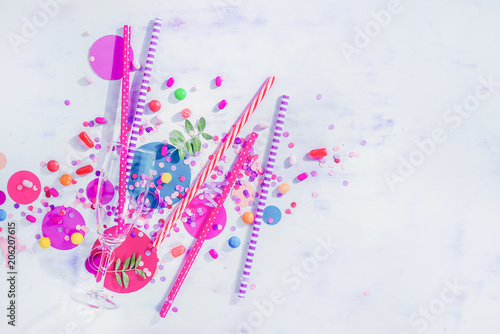 Party concept with bar supplies, colorful flat lay with copy space. Tall cocktail glass with straws, candies, sweets and confetti.