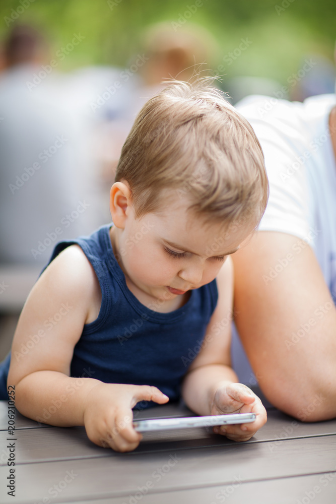 little boy sits next to dad and is highly concentrated with a cell phone in his hands little boy sits next to dad and is highly concentrated with a cell phone in his hands