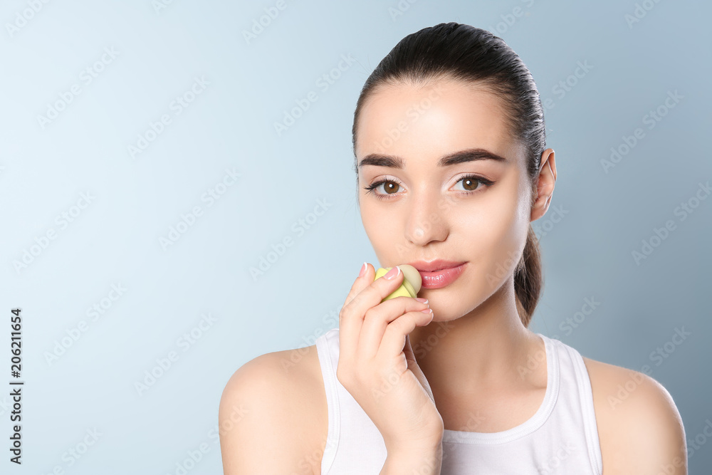 Young woman applying balm on her lips against color background Young woman applying balm on her lips against color background