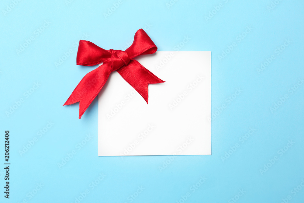 Blank gift tag with satin ribbon on color background, top view