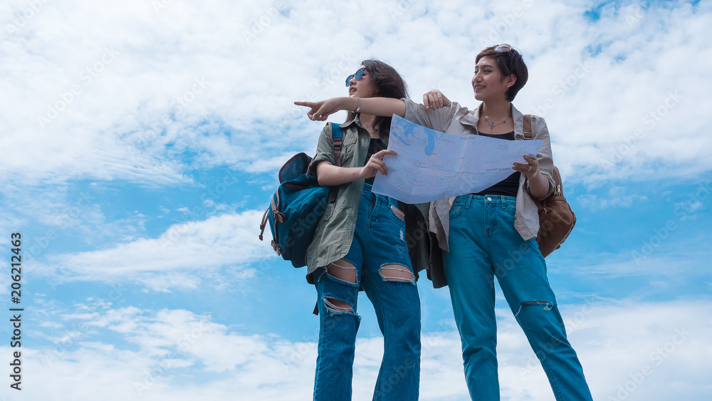 Two young traveler girl looking at the map finding destination with blue sky background
