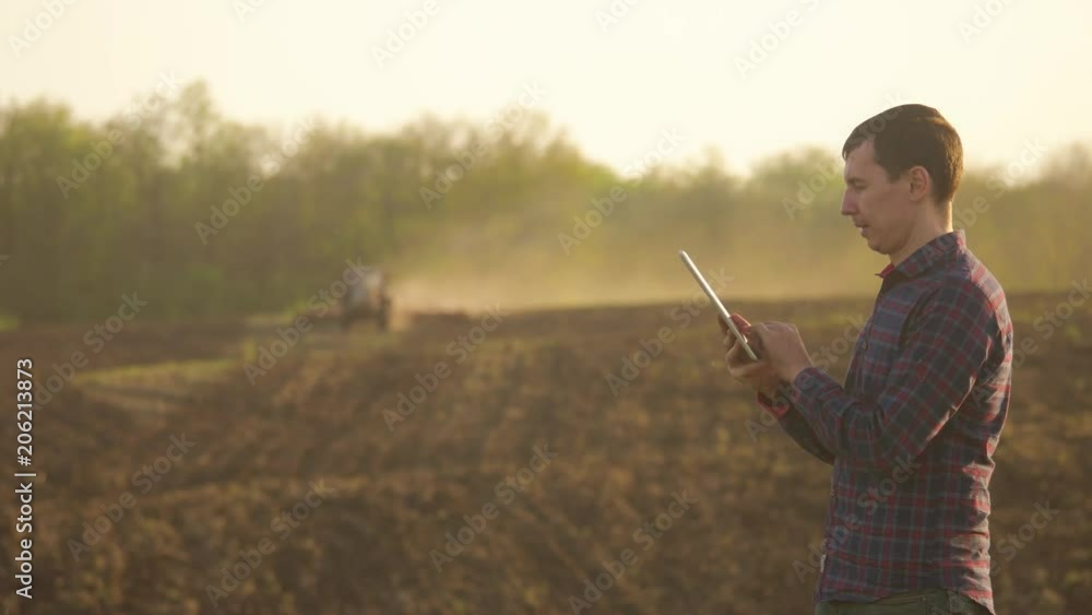 Farmer man read or analysis a report in tablet computer on a agriculture field with vintage tone on a sunlight. the tractor plows a field agriculture concept. Concept ecology . Smart farming lifestyle Farmer man read or analysis a report in tablet computer on a agriculture field with vintage tone on a sunlight. the tractor plows a field agriculture concept. Concept ecology . Smart farming lifestyle