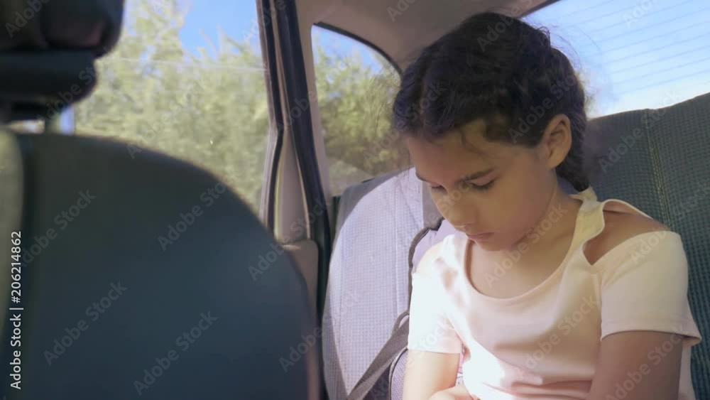 sad girl bored sitting in the car in the back seat travel. little girl bored in the car. concept long motion journey