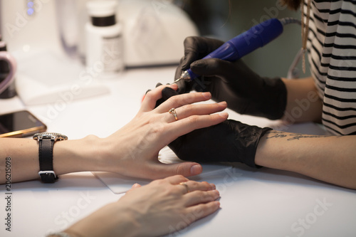 Manicure in process.Closeup shot of a woman in a nail salon receiving a manicure by a beautician with nail file. Woman getting nail manicure. Beautician file nails to a customer.