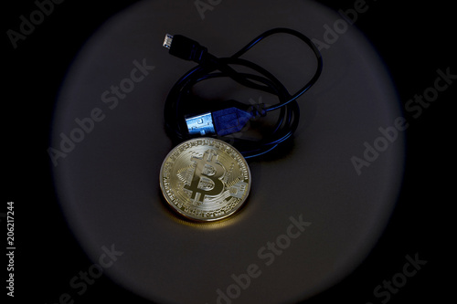 Digital kriptonite bitcoin with a USB cable on a bronze background.
