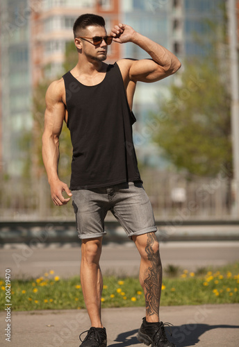 View of young muscular man wearing black t-shirt and jeans walking on the streets of the modern city. Blurred background.