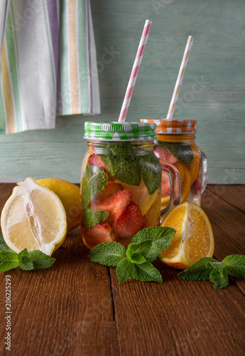 Fresh fruit lemonade with straw in mugs on wooden background and with napkin and mint