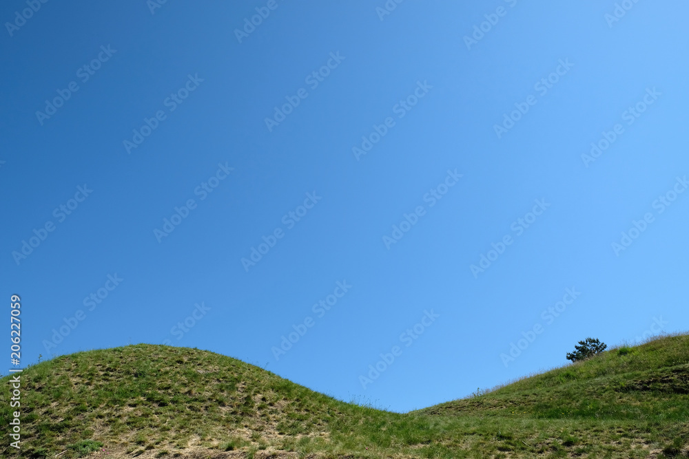 Spitze eines mit Gras bewachsenem doppelhügels mit blauem Himmel im Hintergrund