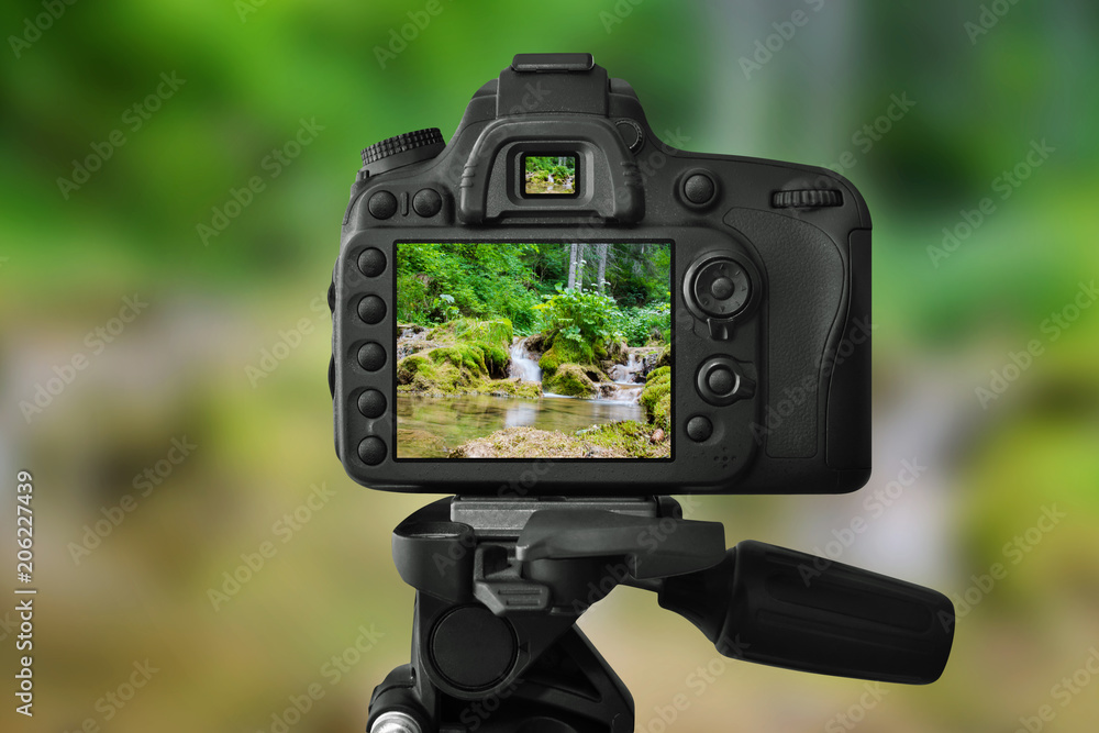 DSLR camera on a tripod is taking a picture of the little waterfall in woods