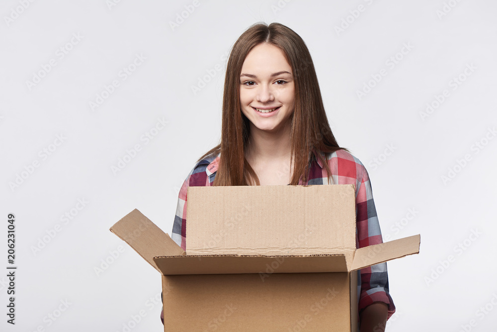 Delivery, relocation and unpacking. Smiling young woman holding carton box looking at camera Delivery, relocation and unpacking. Smiling young woman holding carton box looking at camera