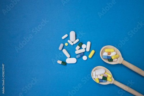 Colorful tablets and pills in wooden spoon. Pharmaceutical pills in wooden spoon on blue background. copy space