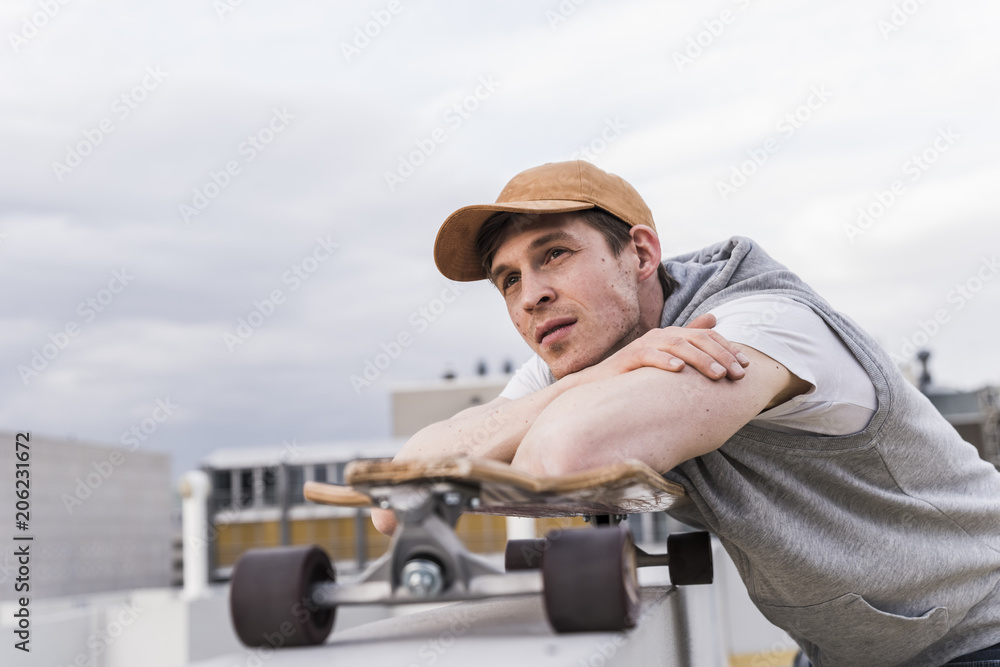 Man with skateboard leaning on a wall looking around Man with skateboard leaning on a wall looking around
