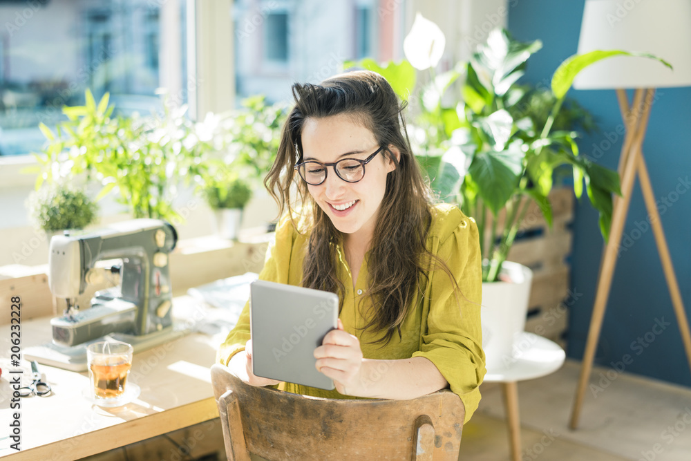 Portrait of smiling fashion designer sitting in her studio using tablet Portrait of smiling fashion designer sitting in her studio using tablet