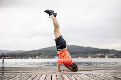 Athlete doing a headstand on wooden deck at the lakeshore photo