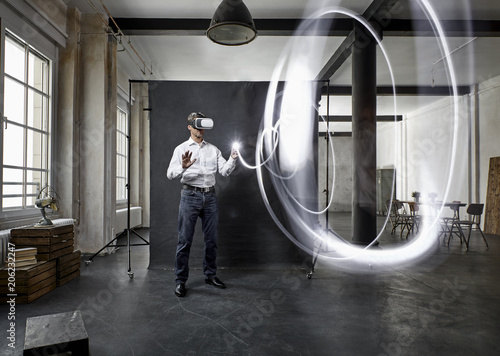 Mature man with vr glasses light painting in front of black backdrop in loft