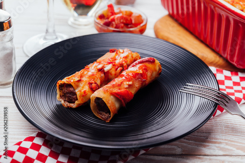 Italian cannelloni stuffed with minced meat and served with tomato sauce and red wine on black plates. photo