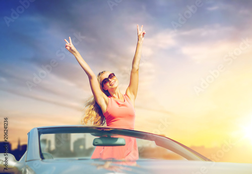 travel, summer holidays, road trip and people concept - happy young woman wearing sunglasses in convertible car enjoying sun