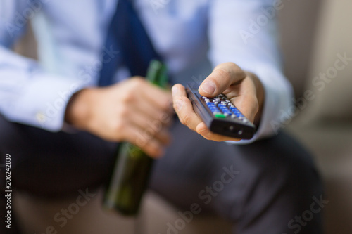 alcoholism, alcohol addiction and people concept - close up of man with tv remote drinking beer