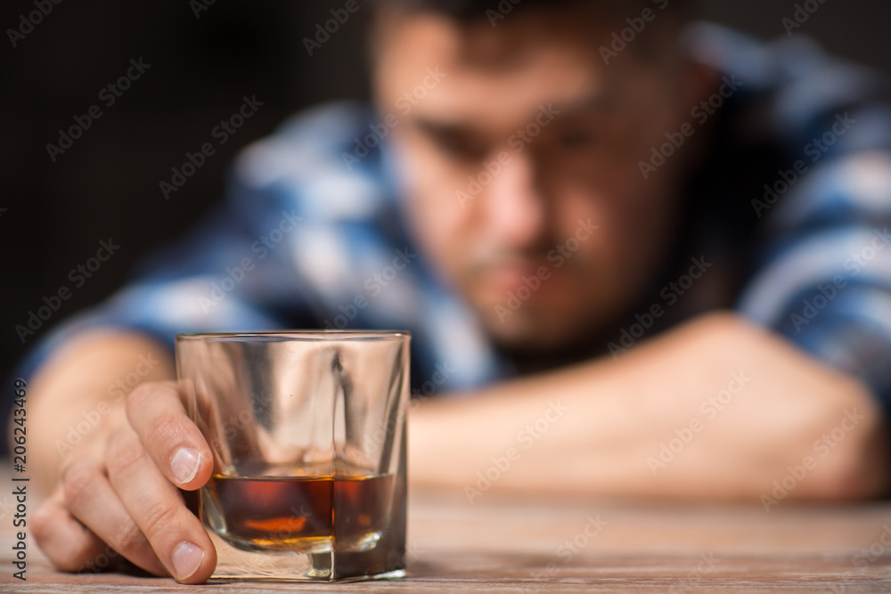 alcoholism, alcohol addiction and people concept - male alcoholic with glass of whiskey lying on table at night alcoholism, alcohol addiction and people concept - male alcoholic with glass of whiskey lying on table at night