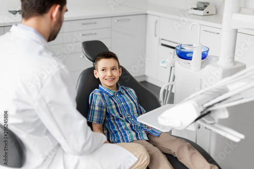 medicine  dentistry and healthcare concept - male dentist talking to kid patient at dental clinic