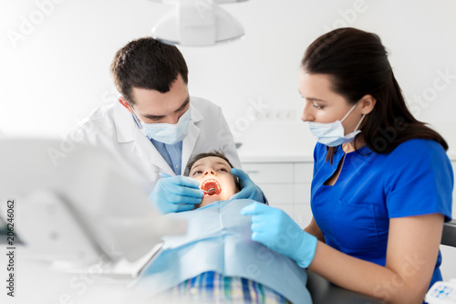 medicine  dentistry and healthcare concept - dentist with mouth mirror checking for kid patient teeth at dental clinic