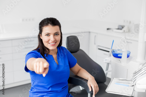 dentistry, medicine and healthcare concept - smiling female dentist or nurse at dental clinic office pointing at you