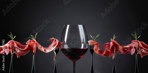 Fototapeta Naklejka Na Ścianę i Meble -  Prosciutto with rosemary and glass of red wine on a dark background.