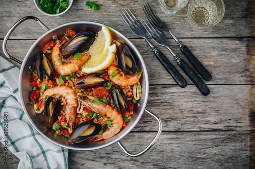 Spanish seafood paella with mussels, shrimps and chorizo sausages in traditional pan on wooden background.