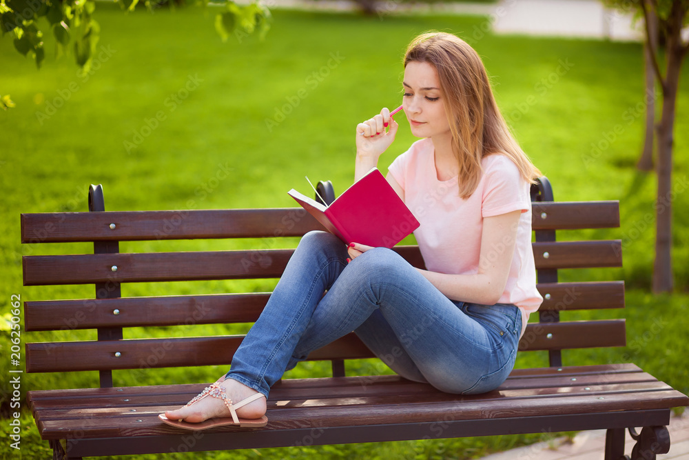 Obraz premium Girl reading a notebook sitting on a bench in the Park