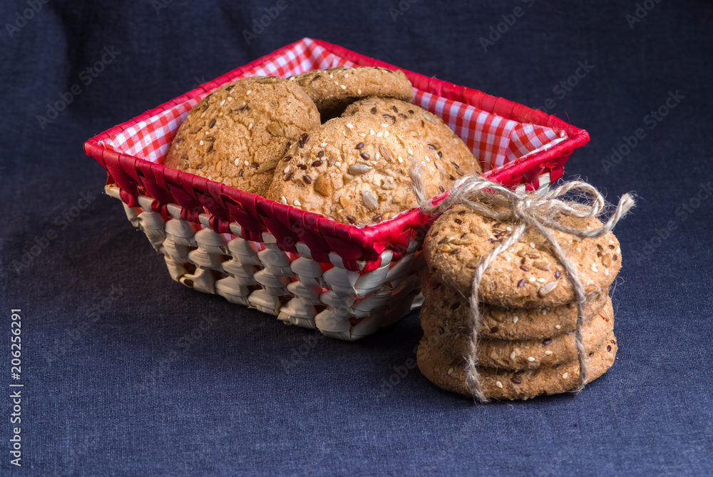 homemade oat cookies with sunflower seeds in and near red checkered basket on dark blue background