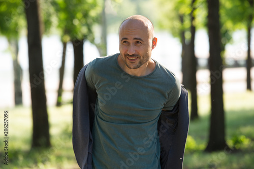 bald bearded man smiles and looks away and takes off his jacket.