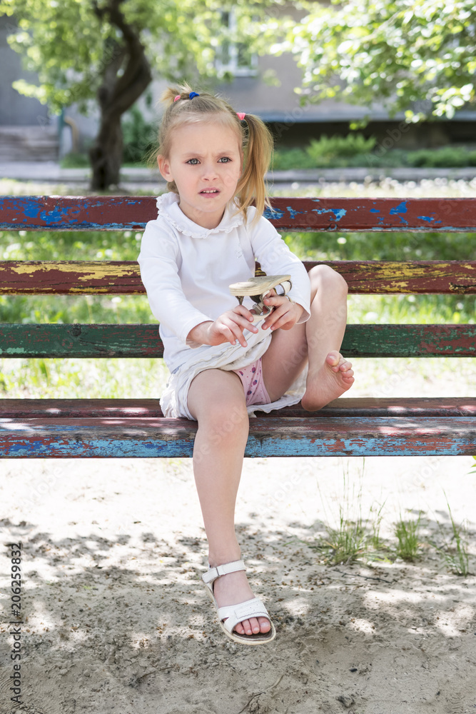 Beautiful little girl sitting on an old bench shakes the sand out of ...